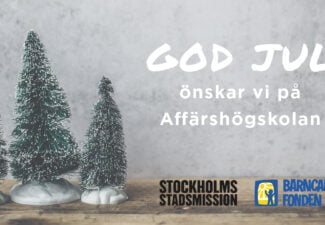 Små plastgranar på träskiva med god jul-hälsning och logotyper för Stockholms Stadsmission och Barncancerfonden