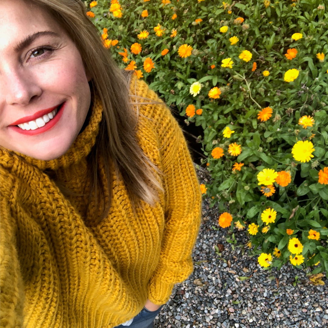Selfie på Hanna Dalme i rött läppsift med gröna växter och gula blommor i bakgrunden