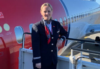Emilia Lindeberg iklädd flygvärdinneuniform bredvid ett stort rödvitt flygplan