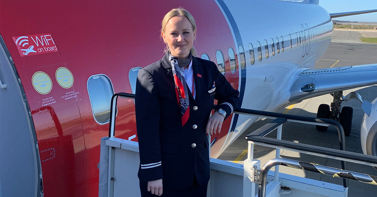 Emilia Lindeberg iklädd flygvärdinneuniform bredvid ett stort rödvitt flygplan