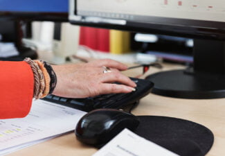 Närbild på skrivbord, datorskärm och en kvinnlig hand som skriver på tangentbord
