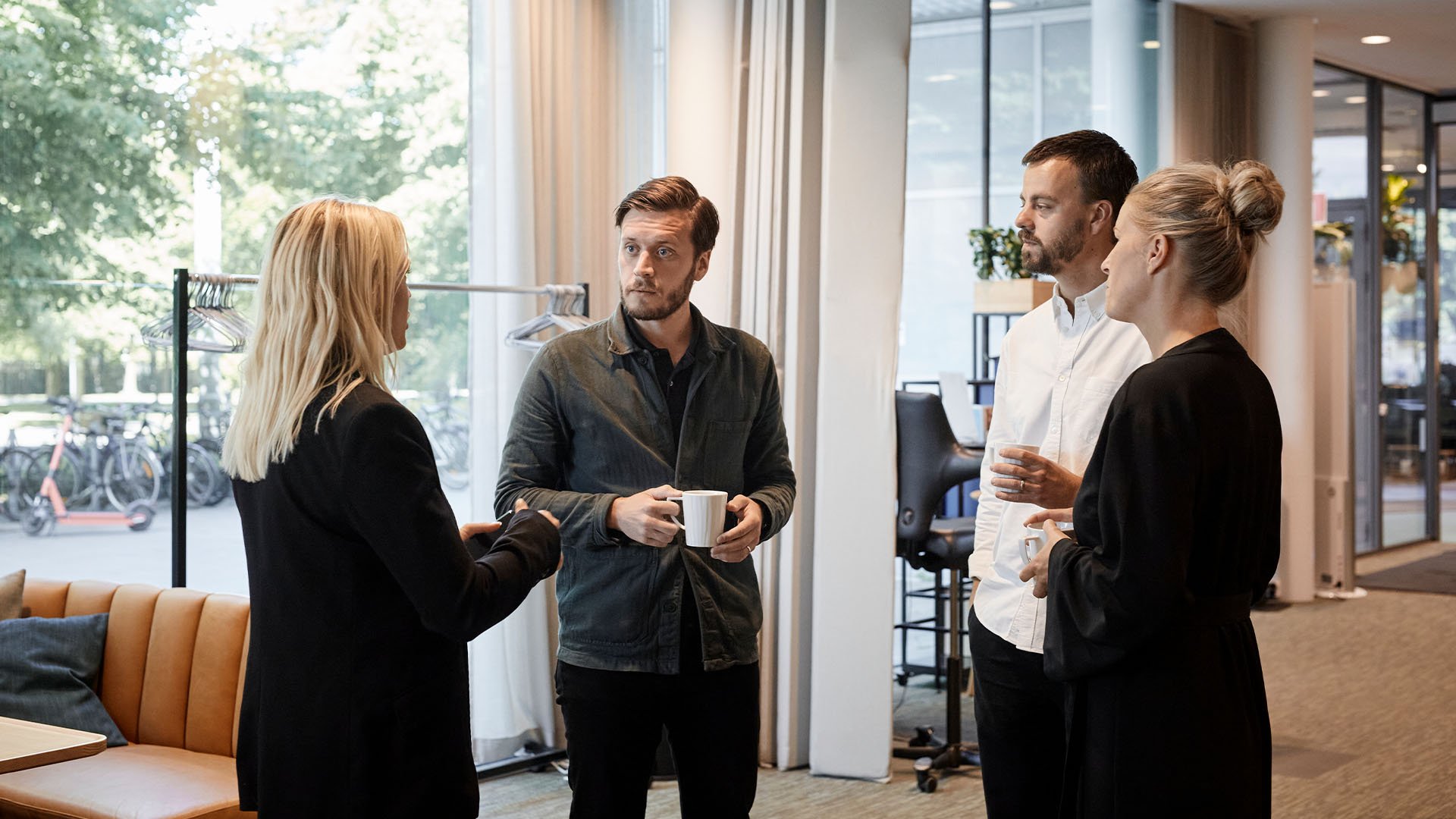 Fyra kollegor som står och samtalar med varsin kaffekopp i handen i kontorsmiljö