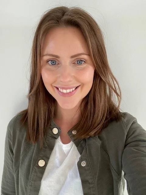 Porträtt av en leende kvinna, Viktoria Bergh, med långt brunt hår, iförd en grön jacka och vit tröja, framför en neutral ljus bakgrund.