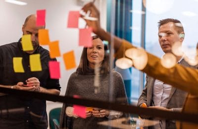 En grupp personer samarbetar vid en glasvägg fylld med färgglada post-it-lappar under en workshop.