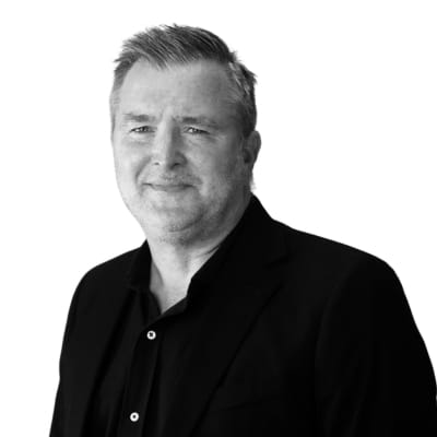Porträttfoto i svartvitt av Andreas Wieselqvist, utbildningsledare. En man med kort, ljust hår och kavaj, som ler svagt mot kameran.