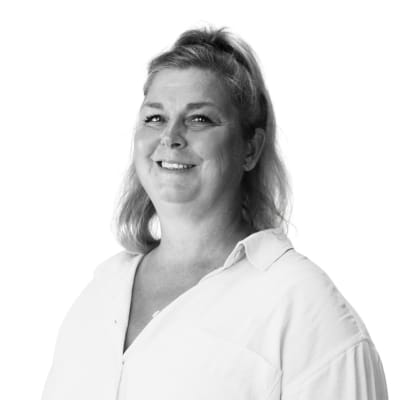 Porträttfoto i svartvitt av Jenny Samuelsson, utbildningsledare. En kvinna med axellångt blont hår och ljus skjorta, som ler mot kameran.