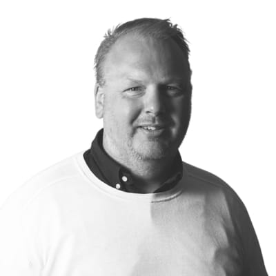 En porträttbild på Markus Karlsson, utbildningsledare på Affärshögskolan. Han är en man som ler, klädd i en ljus tröja och en skjorta under. Bilden är i svartvitt med en vit bakgrund.